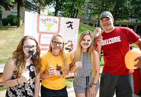 Four ̳ students hold up mustaches on a stick.
